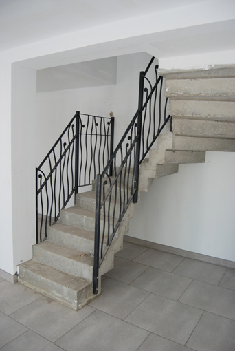 Escalier béton deux quarts tournants avec rambarde en fer forgé vu d'en bas